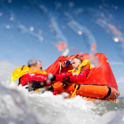Two people in a red inflatable raft navigating rapids with water splashing around.